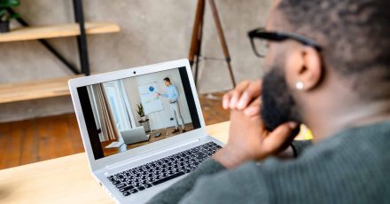 A black guy watching webinars online Learning online, webinar, online video classes. Focused African-American guy is watching online video lectures, male teacher with a flip chart on the laptop screen, view from the back.